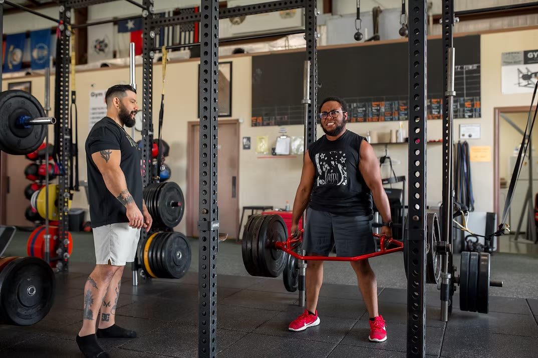 A client lifting a loaded trap bar in the rack while Martin coaches